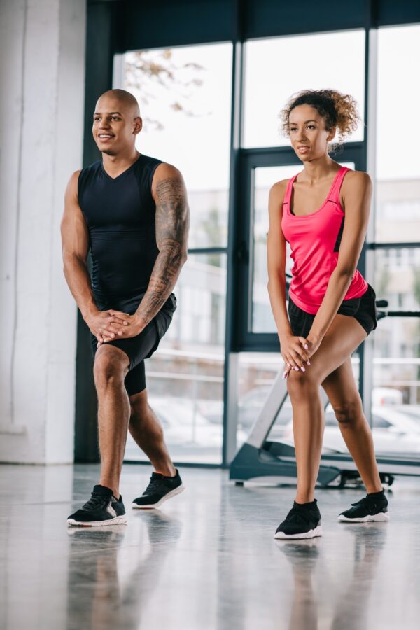 smiling african american couple of athletes doing exercise at gym