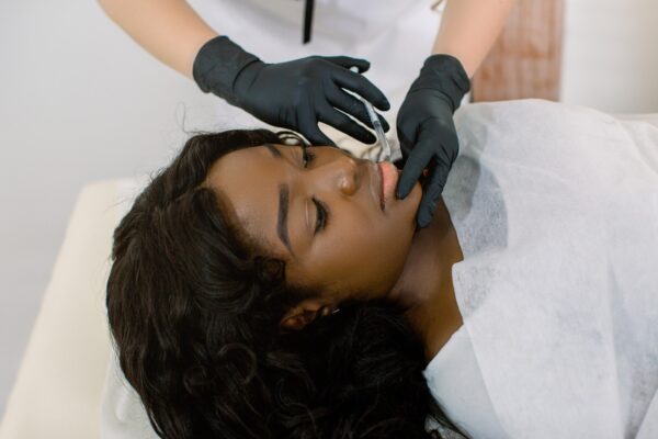 Close up of hands of female cosmetologist making botox injection in female lips, holding syringe